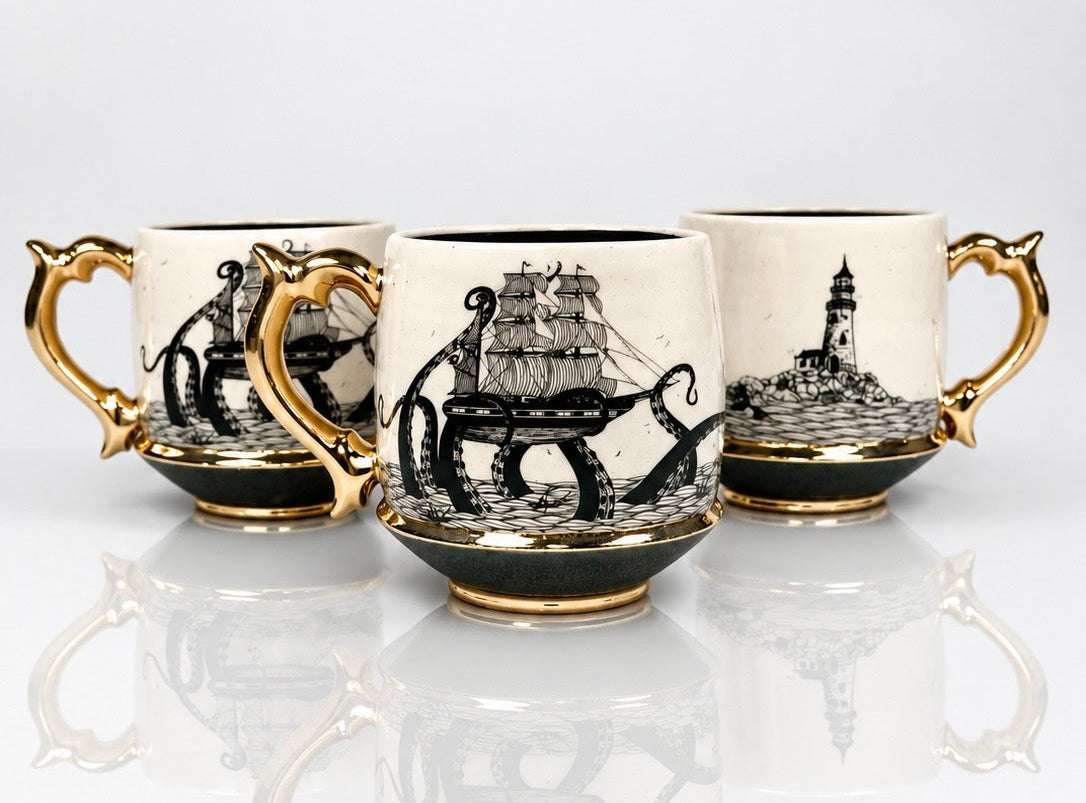 Three ceramic mugs with ornate gold handles and bases, decorated with black nautical illustrations including a ship, octopus, and lighthouse, on a white background with reflections.